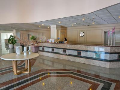 Vestíbulo luminoso de hotel con recepción, mesa redonda y plantas.