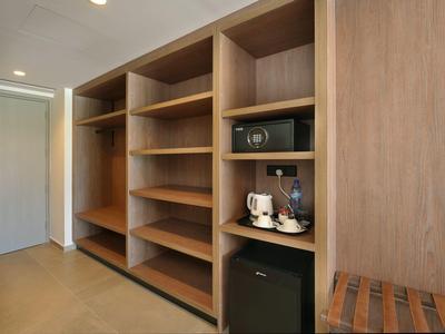 Offener Holzschrank mit Regalen, Safe, Minibar und Kaffeemaschine in einem Hotelzimmer.