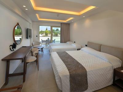 Helles Hotelzimmer mit zwei Doppelbetten, Schreibtisch und Blick auf eine Terrasse mit Pool.