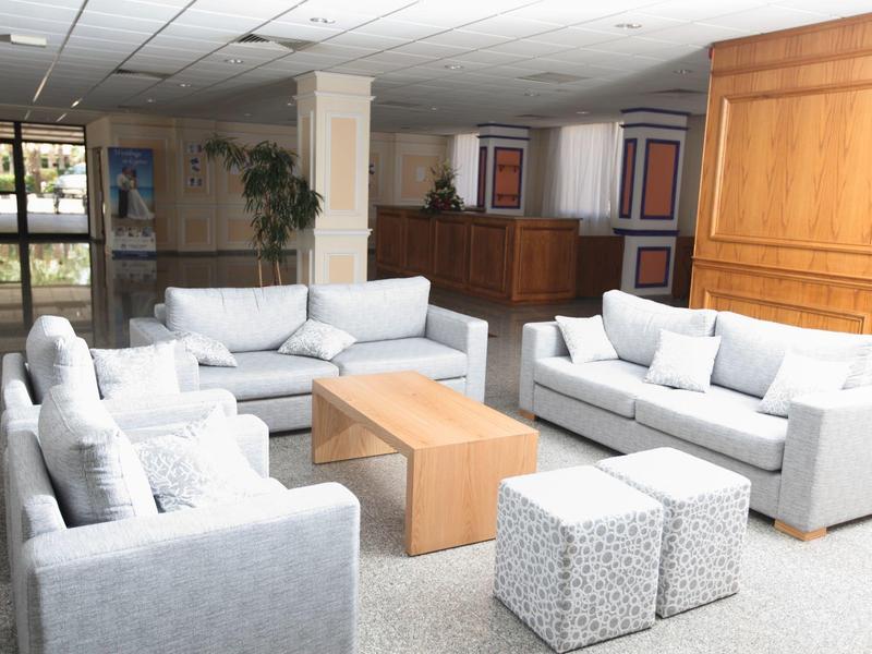 Helles Hotelzimmer mit drei grauen Sofas, Couchtisch und gepolsterten Hockern.
