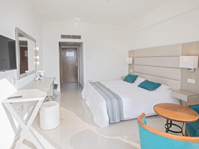 Helles Hotelzimmer mit Doppelbett, Schreibtisch, TV und modernem Sitzbereich.