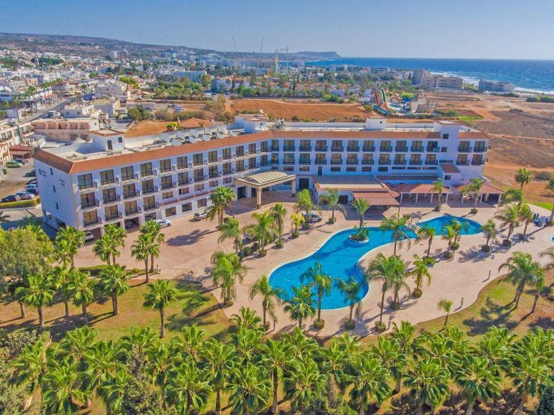 Großes Hotel mit geschwungenem Pool, Palmen und Blick auf das Meer und die Stadt.