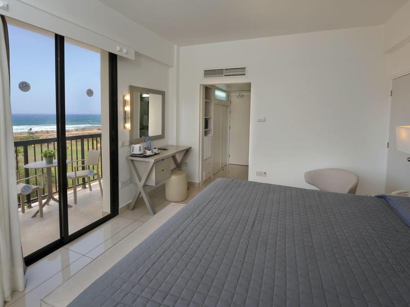 Helles Hotelzimmer mit großem Bett, Balkon und Blick auf das Meer.