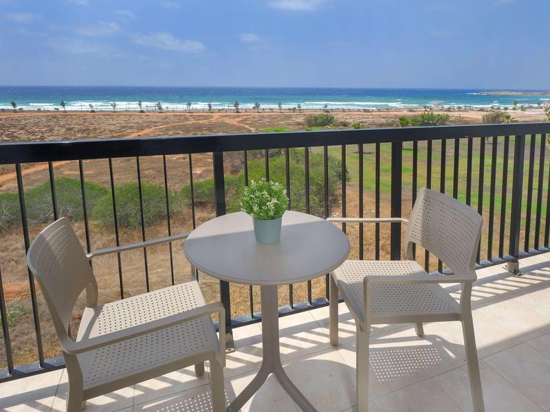 Balkon mit kleinem weißem Tisch, zwei Stühlen und Meerblick im Hintergrund.