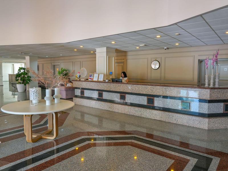 Hotel-Empfang mit Rezeption, rundem Tisch und Blumendekoration in hellem Eingangsbereich.