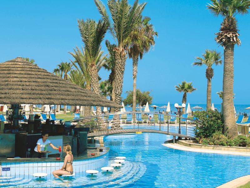 Großer Pool mit blauem Wasser, Palmen und Sonnenschirmen unter klarem Himmel.