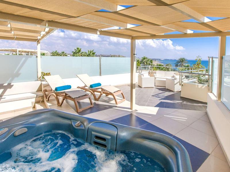 Moderne Terrasse mit Whirlpool, Liegestühlen und Lounge-Bereich unter Holzpergola bei Sonnenschein.