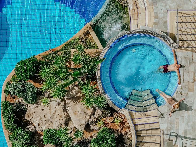 Runder Pool mit bläulichem Wasser und Sonnenschirm neben Steinpflanzen und Treppen.