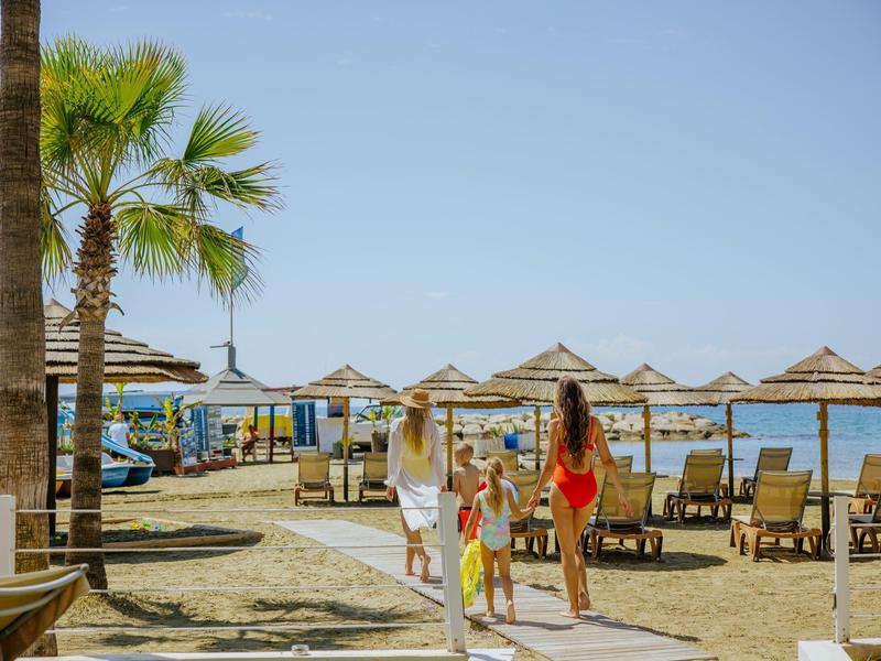 Strand mit Palmen, Sonnenschirmen, Liegen und Menschen bei Sonnenschein und klarem Himmel.