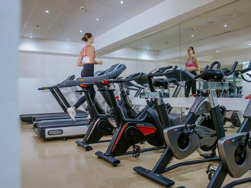Ein heller Fitnessraum mit Laufbändern und Fahrrädern, Frau trainiert auf einem Laufband.