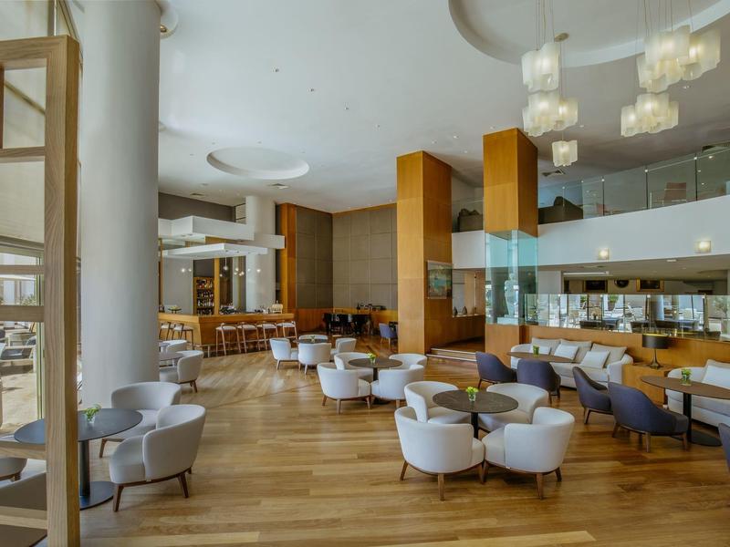 Großer, heller Gastraum mit Holzboden, weißen Sesseln und modernem Design in warmen Farben.