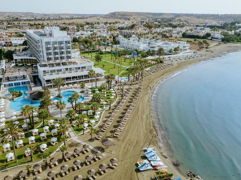 Große Küstenanlage mit Hotel, vielen Palmen, Pools, Liegen und Sandstrand am ruhigen Meerufer.