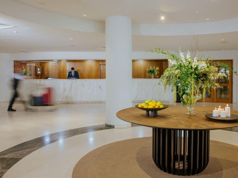 Moderne Hotellobby mit runder Empfangstheke, großem Blumengesteck und warmem Licht.