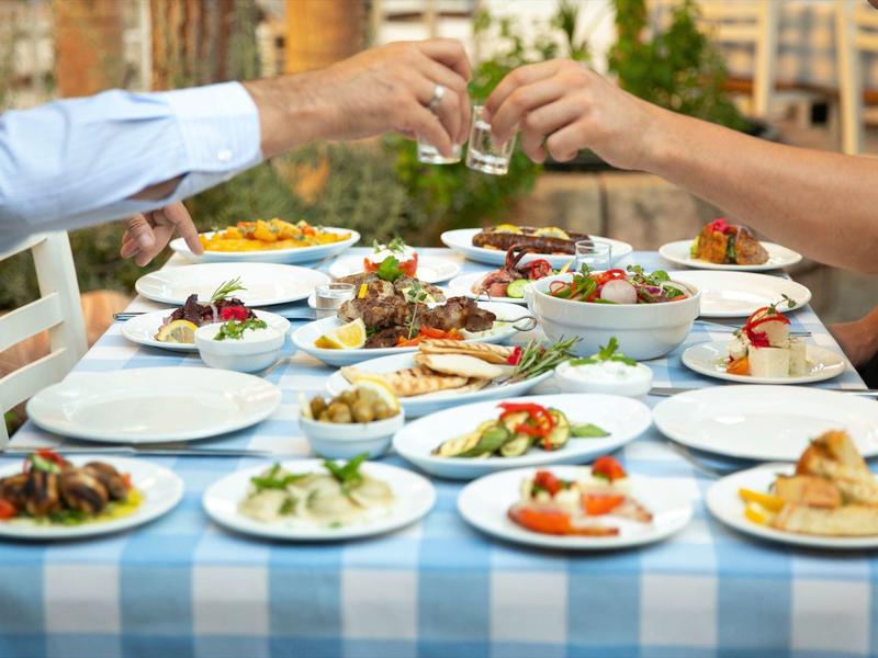 Eine gedeckte Tafel mit vielfältigen Vorspeisen und zwei Menschen stoßen mit Gläsern an.
