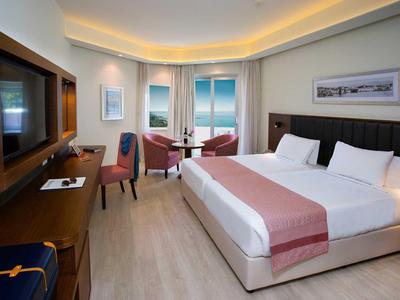 Modern hotel room with large bed, sea view, seating area, and television.