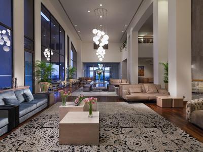Spacious hotel lobby with modern sofas, decorative chandelier, and patterned rug.