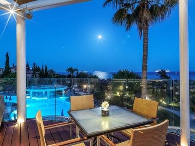 Evening patio with outdoor dining table, chairs, pool, palm tree, and ocean view under moonlight.