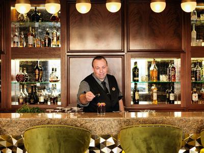 Bartender behind a polished marble bar with shelves of liquor bottles, serving a drink.