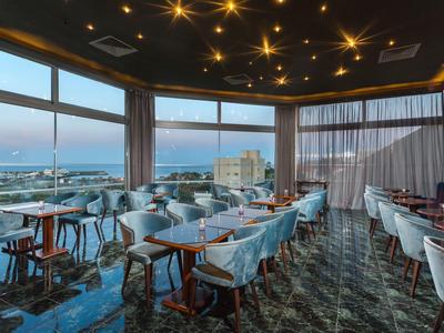 Spacious restaurant with ocean views, modern decor, and ceiling lights during sunset.