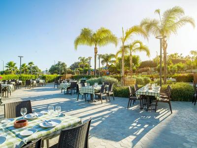 Restaurante al aire libre con mesas preparadas junto a palmeras en un día soleado