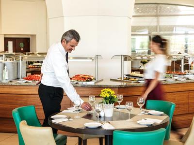 Hotel dining area with round table, teal chairs, waiter serving, buffet background.