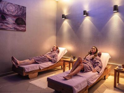 Two women relaxing on lounge chairs in a softly lit spa room.