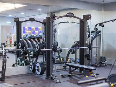 Gimnasio moderno con equipos de entrenamiento y espejos en una habitación luminosa.