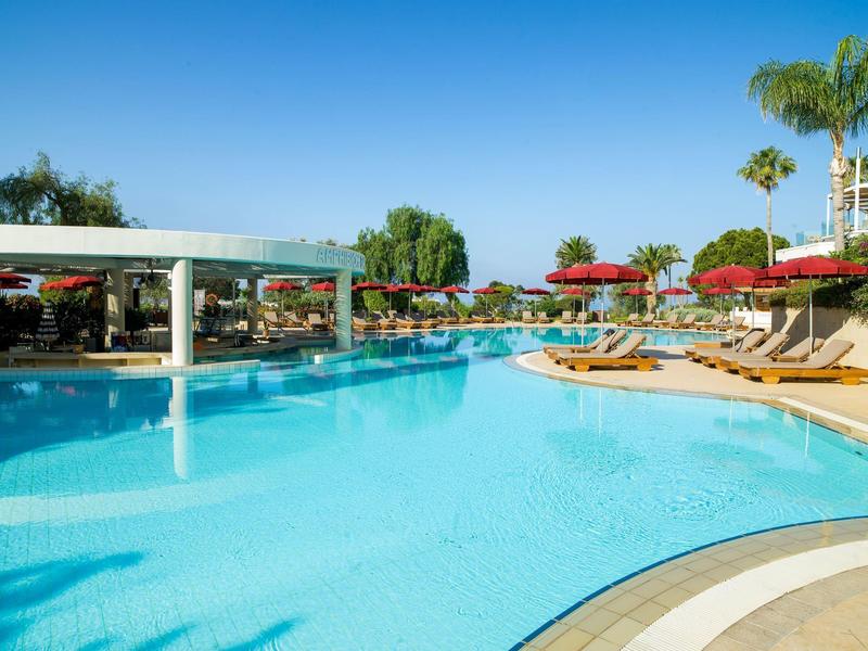 Outdoor hotel pool with sun loungers and red umbrellas under clear blue sky