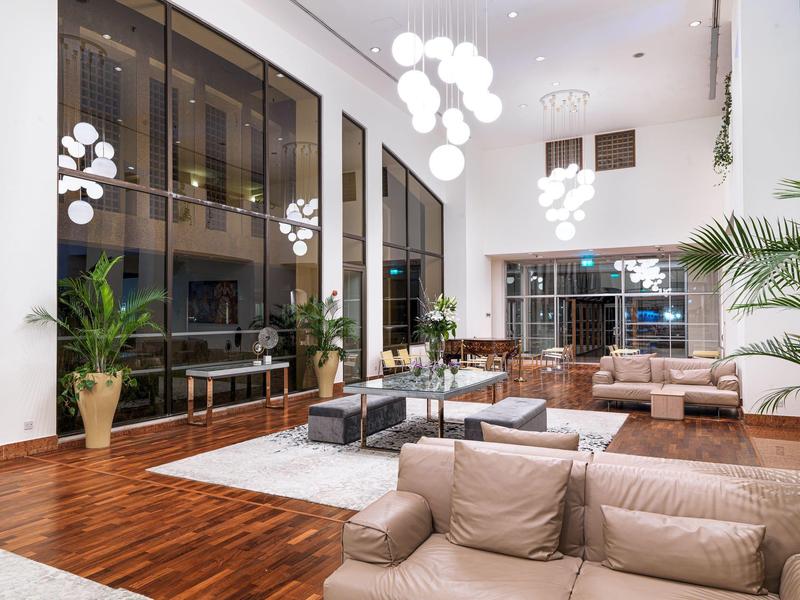 Spacious hotel lobby with modern sofas, large windows, wooden floors, and decorative lighting.