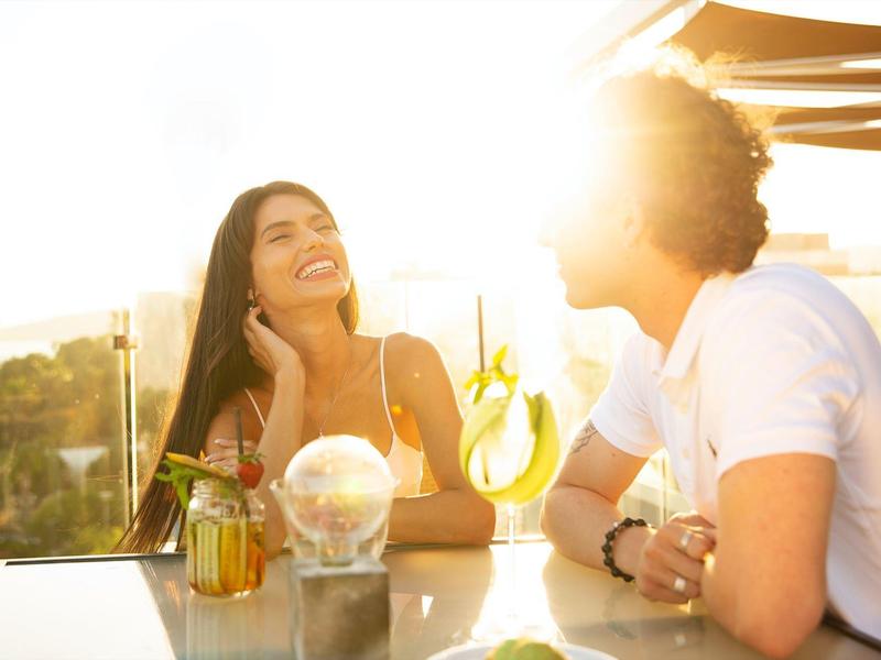 Couple enjoying a sunny rooftop drink with city views in the background.