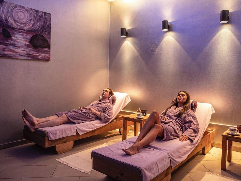 Two women relaxing on lounge chairs in a softly lit spa room.