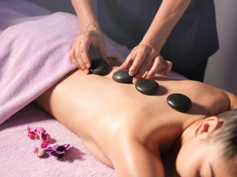 Person receiving hot stone massage on back with orchid flowers nearby.