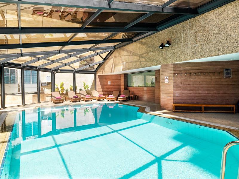 Indoor pool with large windows and lounge chairs in a sunlit room.