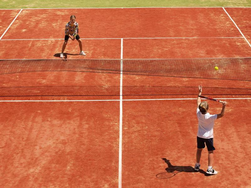 Two players on a clay tennis court with one serving the ball.
