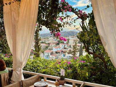 Terrasse mit weißen Vorhängen, Tisch mit Tellern, Blick auf bunte Häuser und Berge im Hintergrund.