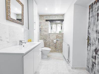 Bagno luminoso con mobile lavabo bianco, specchio, WC e parete in pietra con finestra.