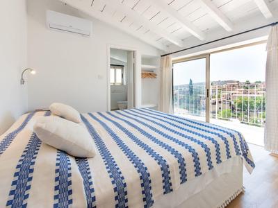 Helles Schlafzimmer mit blau-weiß gestreiftem Bett, großen Fenstern und Blick auf einen Balkon.