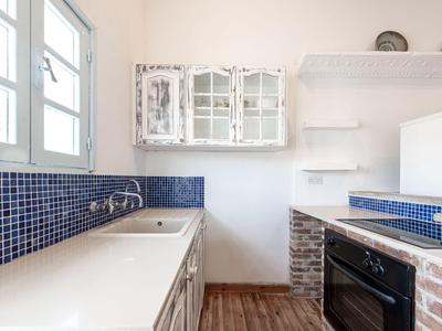 Piccola cucina con piastrelle blu, armadietti bianchi e pavimento in legno in una camera d'hotel.