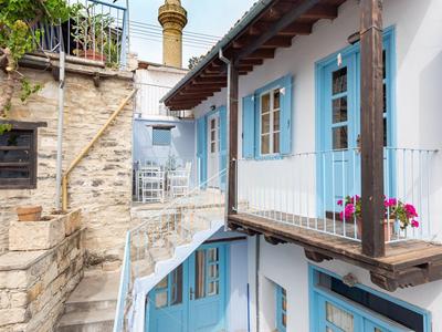 Ein idyllisches weiß-blaues Haus mit Balkon und einer steinernen Treppe unter blauem Himmel.