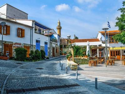 Malersicher Platz mit Kopfsteinpflaster, weiß getünchten Gebäuden und einer offenen Terrasse unter blauem Himmel.