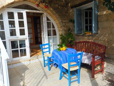 Gemütliche Terrasse mit blauem Tisch, Stühlen und rustikalem Holzbett an Steinwand.