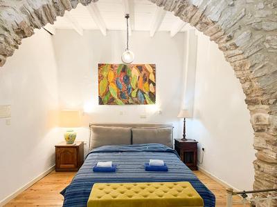 Schlafzimmer mit Doppelbett unter einem Steinbogen, Garderoben mit Nachttischen und Lampen, bunte Wandkunst.