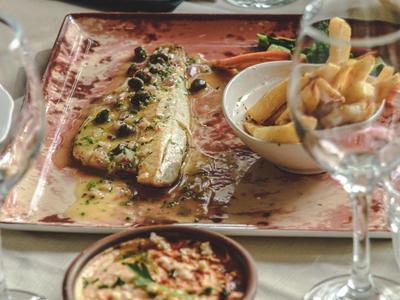 Ein gedeckter Tisch mit mediterranen Gerichten, darunter gegrillter Fisch und Dips.