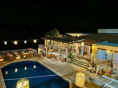 Beleuchteter Poolbereich mit Sitzgelegenheiten und einem gemütlichen Haus bei Nacht.