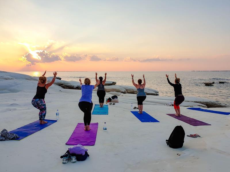 Gruppe praktiziert Yoga auf einer Terrasse mit Blick auf das Meer bei Sonnenuntergang.