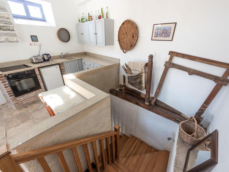 Helle Küche mit weißen Schränken, Holztreppe und antiken Weinpressen an der Wand.