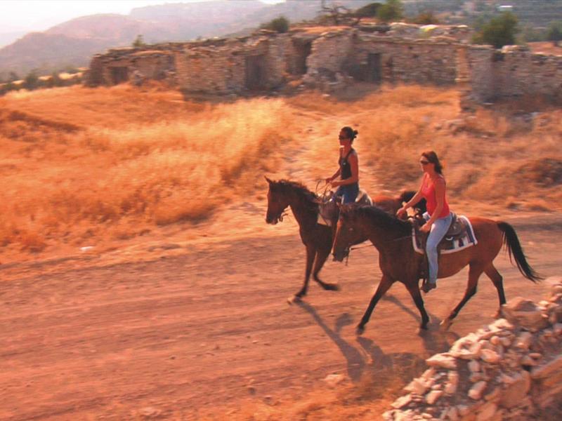 Steinernes Gebäude mit blühenden pinken und weißen Bäumen, Terrasse und Sonnenschirm.