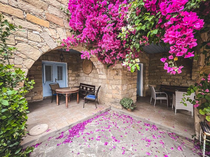 Gemütlicher Innenhof mit Steinmauern, Bänken und leuchtend pinken Blumen.