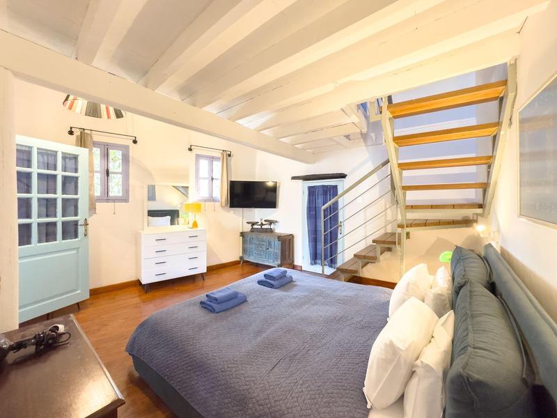 Modernes Schlafzimmer mit grauem Bett, weißen Kommoden und offener Treppe in einem hellen Raum