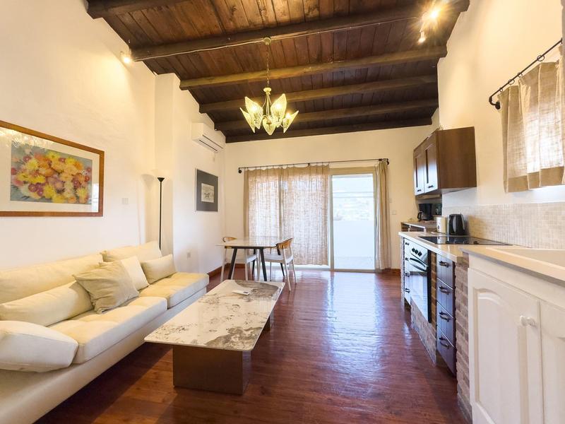 Helles Wohnzimmer mit Holzbalkendecke, weißem Sofa, Marmortisch und Esstisch neben großen Fenstern.